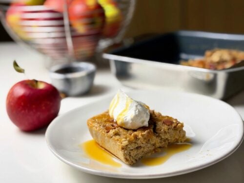 Plated slice of high-protein apple pie baked oatmeal topped with yogurt, cinnamon apples, and syrup