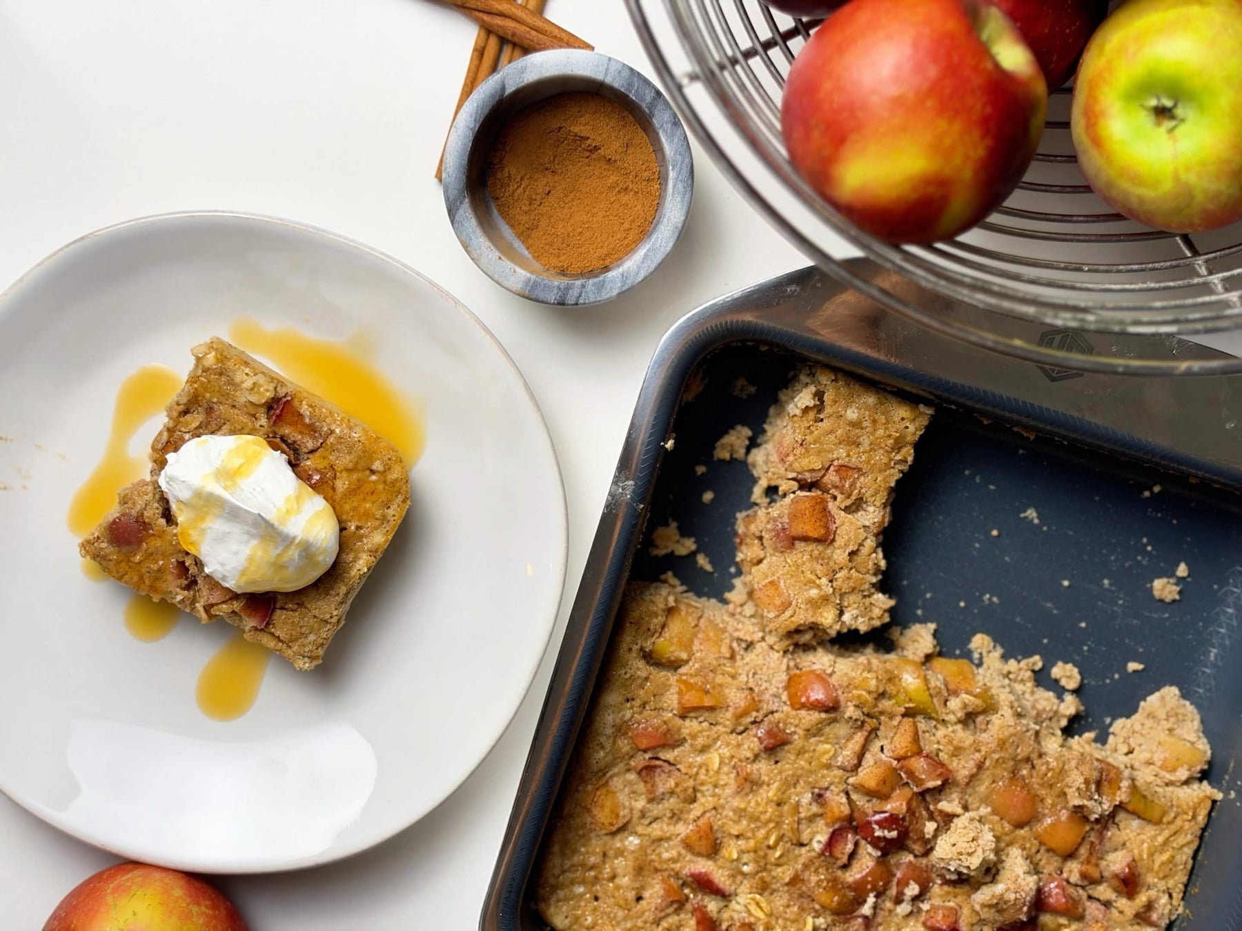Overhead serving scene with a plated apple pie baked oatmeal slice beside the partially served baking pan