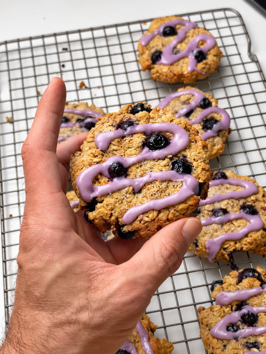 Close-up of a glazed blueberry oatmeal breakfast cookie held over a cooling rack