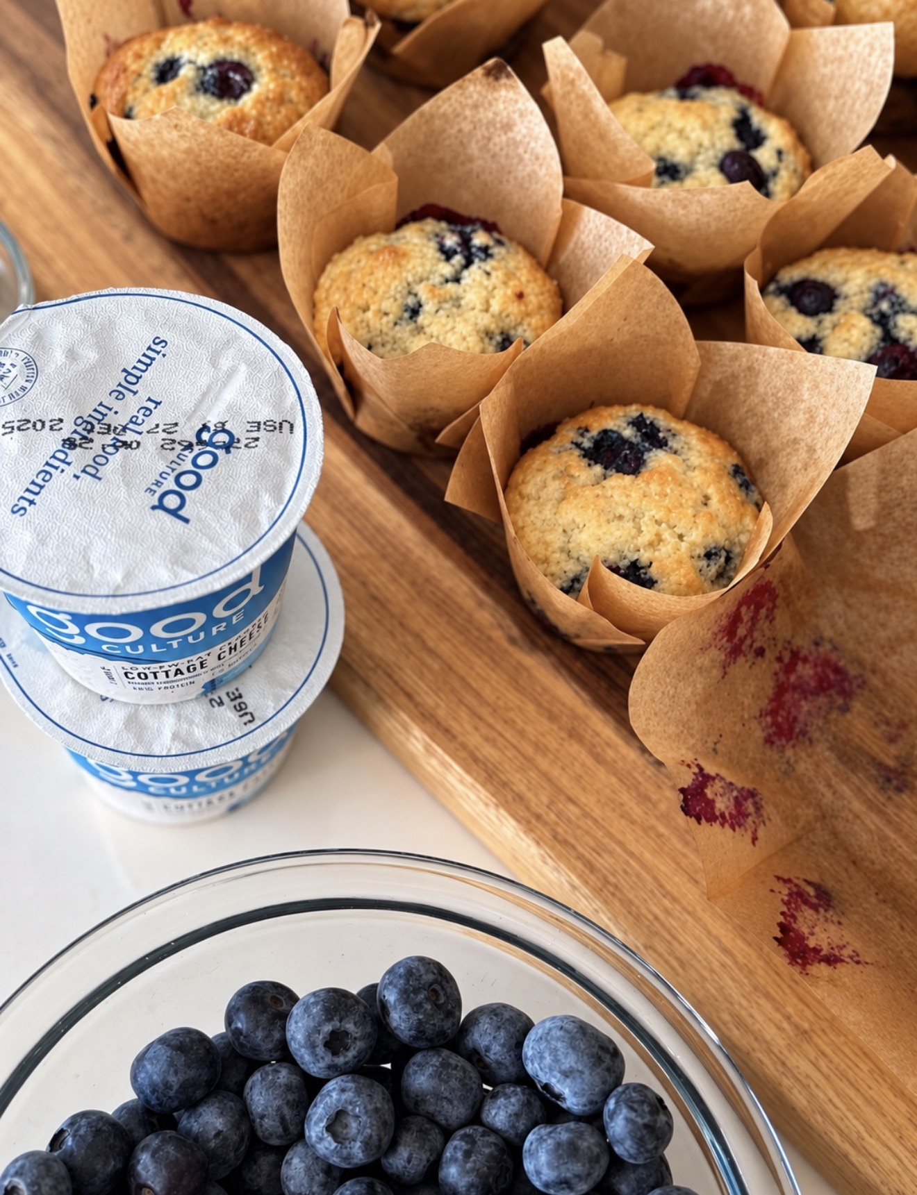 Fresh blueberry cottage cheese muffins beside Good Culture cottage cheese and a bowl of blueberries