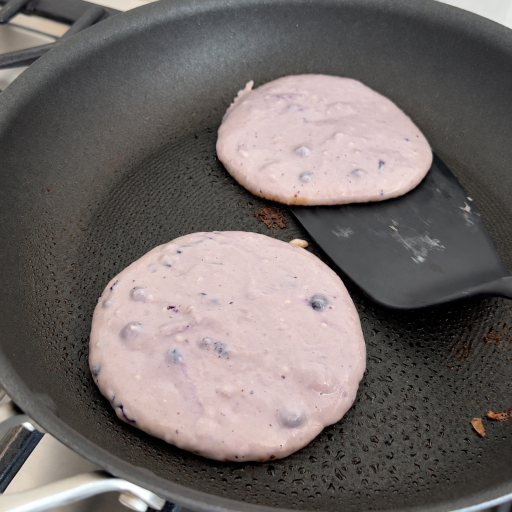 Blueberry pancake batter cooking in a nonstick skillet
