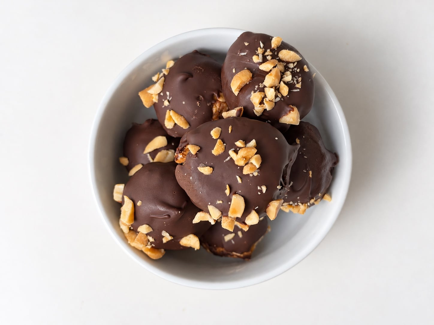 Bowl filled with chocolate peanut butter protein truffles topped with chopped peanuts