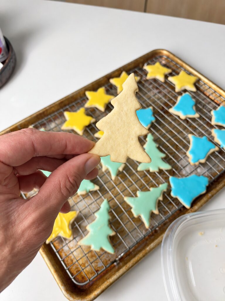 Plain tree-shaped cream cheese sugar cookie held above decorated cookies