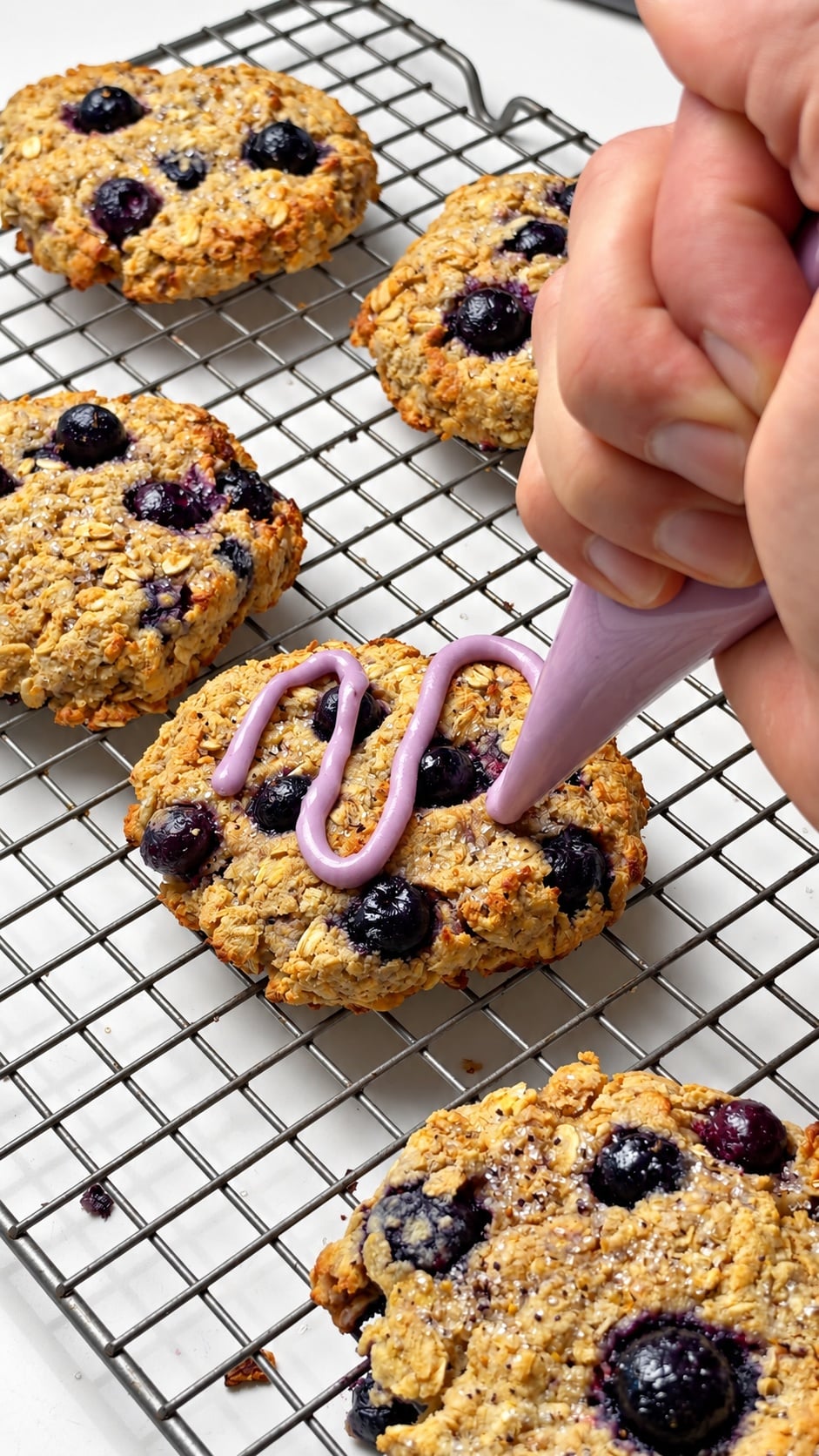 Purple blueberry glaze being drizzled over a blueberry oatmeal breakfast cookie