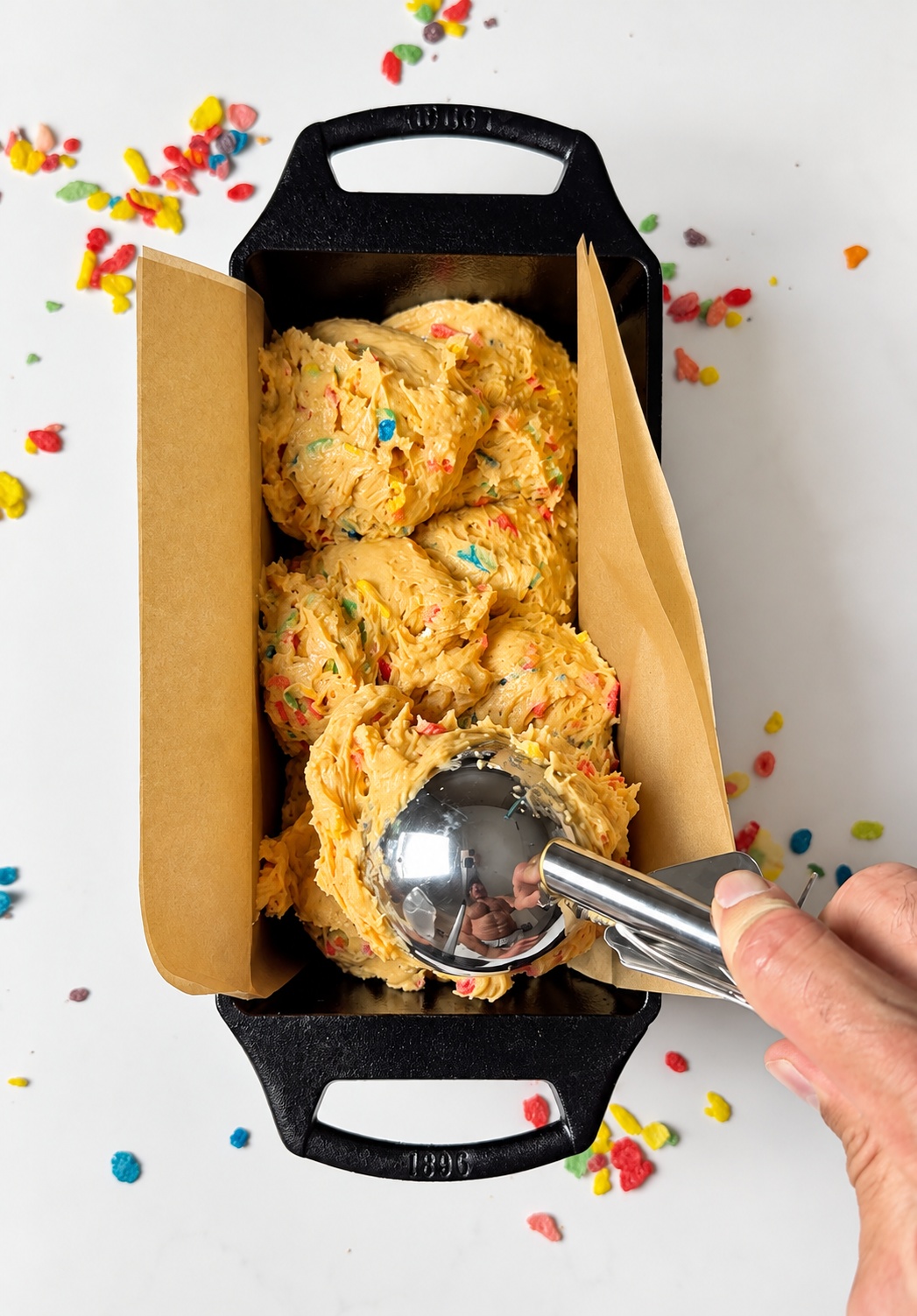 Fruity Pebbles protein loaf cake batter being added to a parchment-lined loaf pan