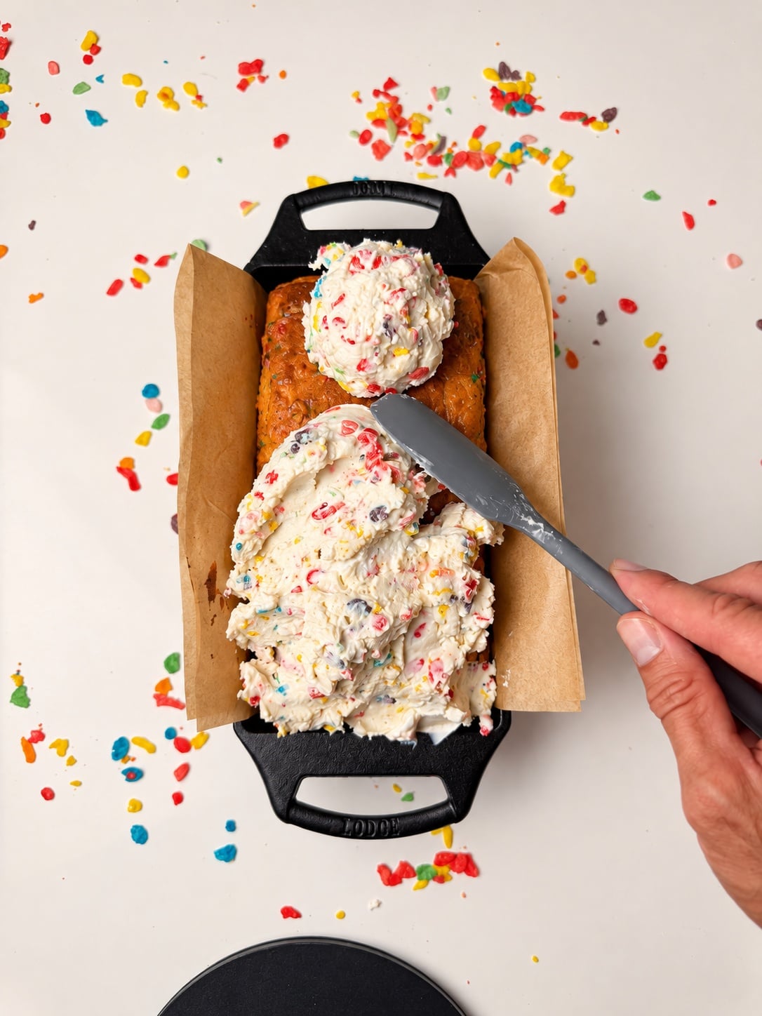 Fluffy yogurt frosting being spread over a Fruity Pebbles protein loaf cake