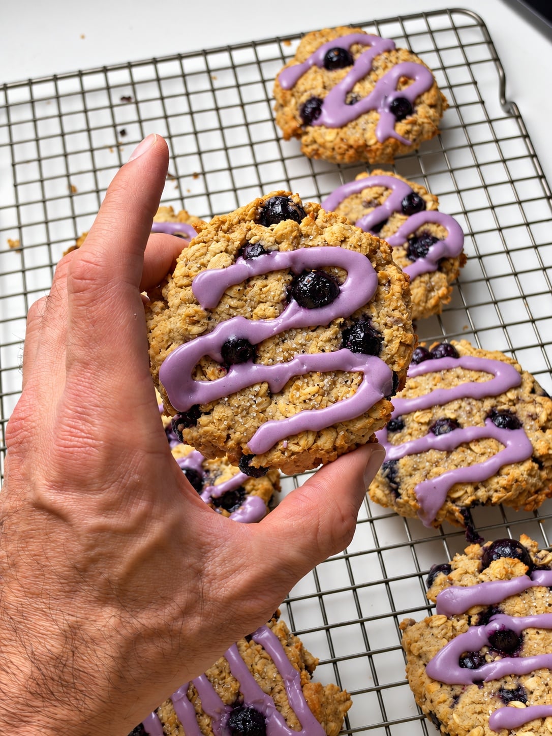 Hand holding a glazed blueberry protein breakfast cookie over a cooling rack