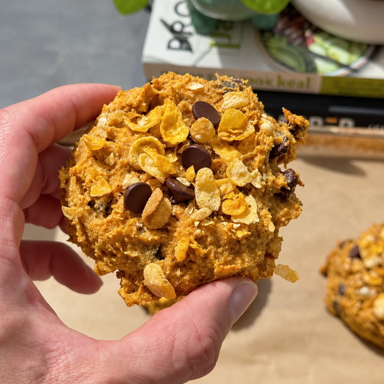 Hand holding an unglazed pumpkin corn flake protein breakfast cookie with chocolate chips