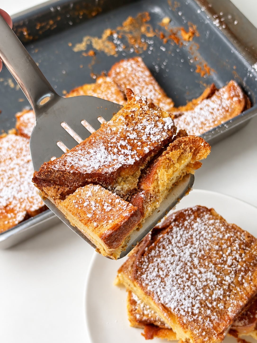 Thick pieces of French toast casserole lifted from the baking pan on a metal spatula.