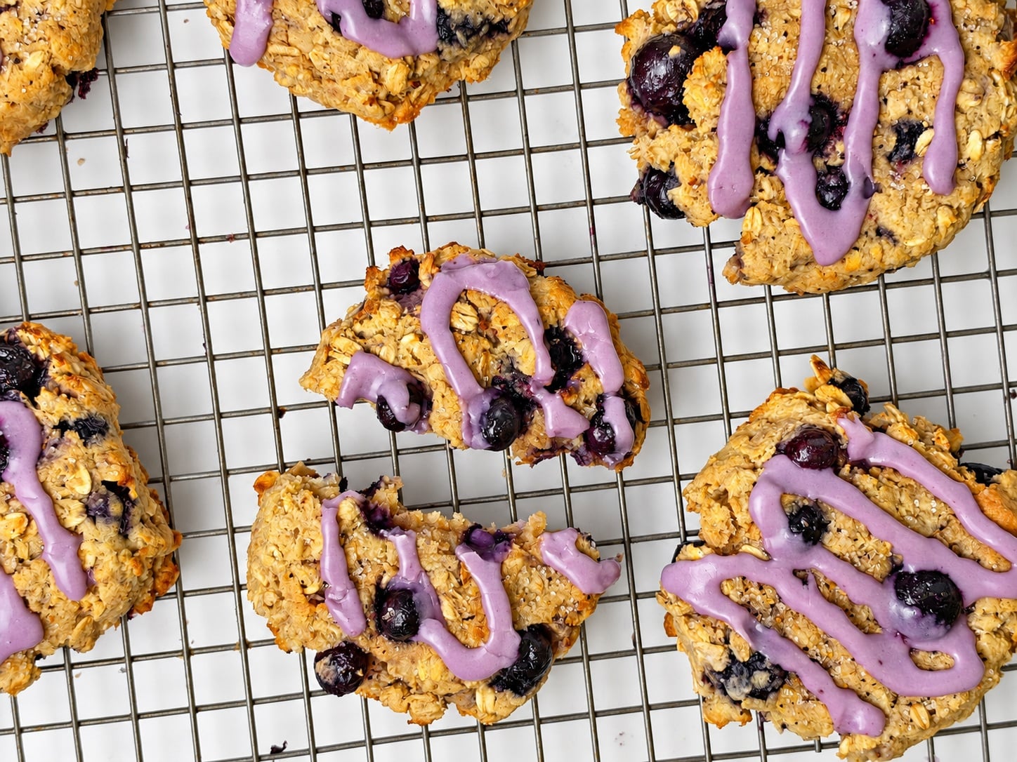 High-protein blueberry oatmeal breakfast cookies with purple blueberry glaze on a cooling rack