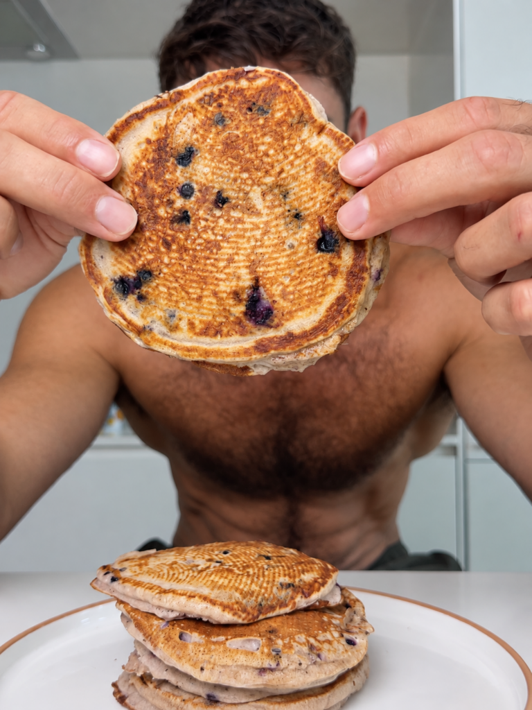Close-up of a golden blueberry pancake held above a stack