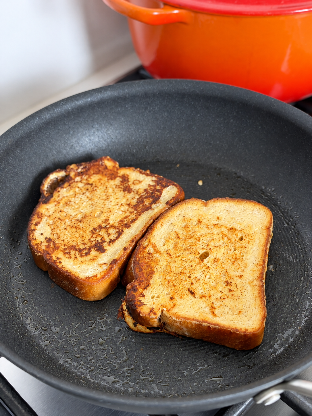 Two slices of high-protein French toast browning in a nonstick skillet.