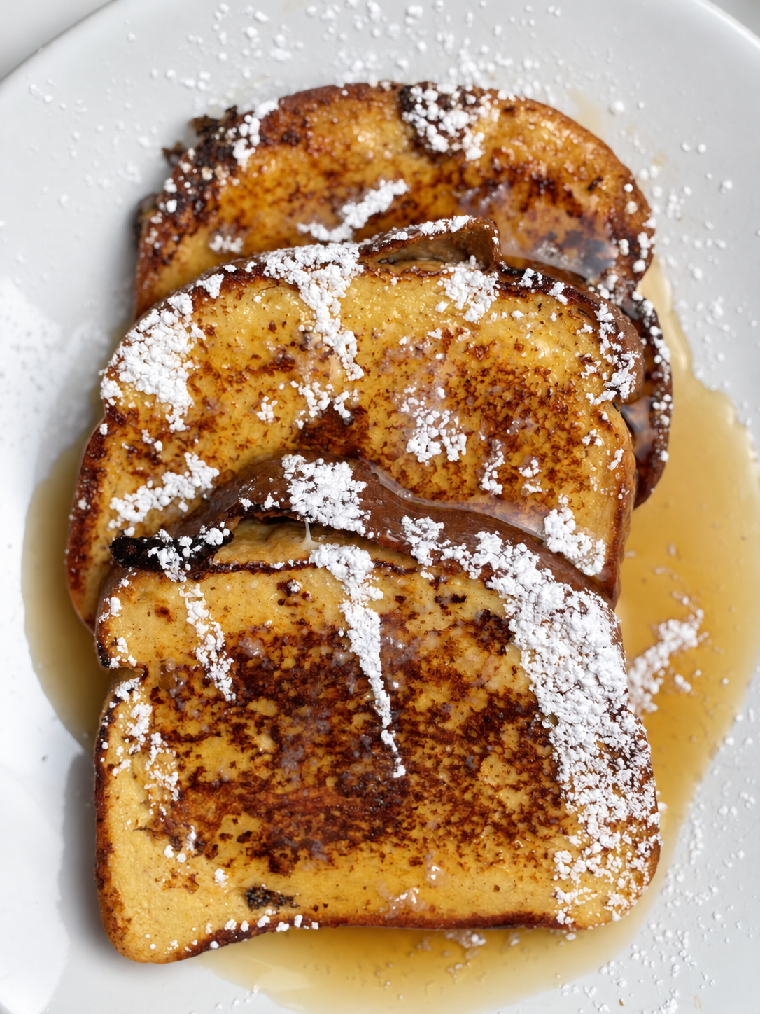 Top view of three browned slices of high-protein French toast with powdered sweetener and syrup.