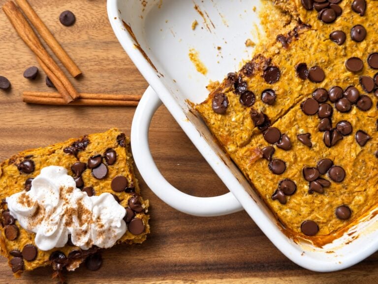 Slice of high-protein pumpkin baked oatmeal topped with whipped cream beside the baking dish