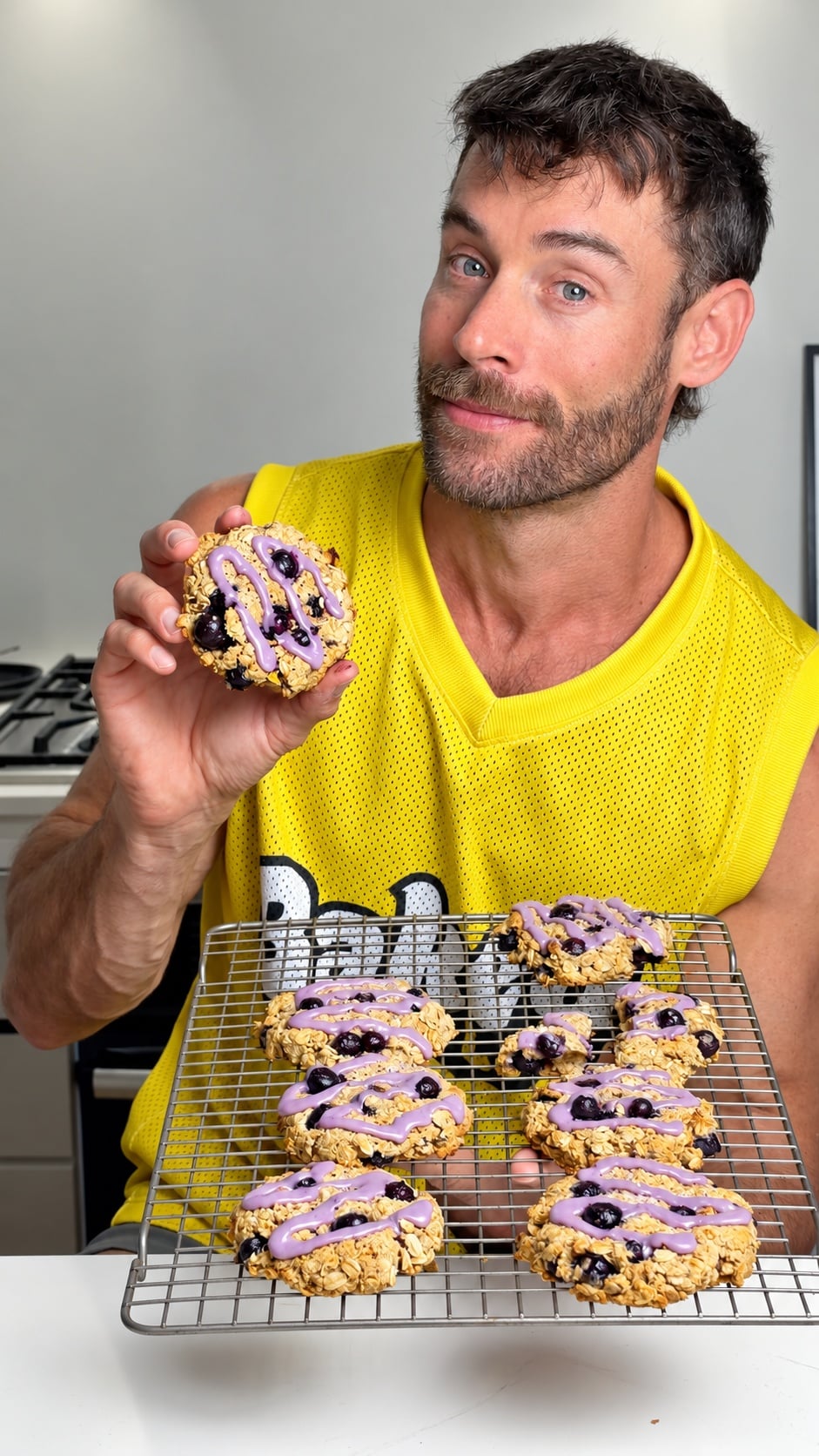 Jacob holding a glazed blueberry breakfast cookie and a cooling rack filled with cookies