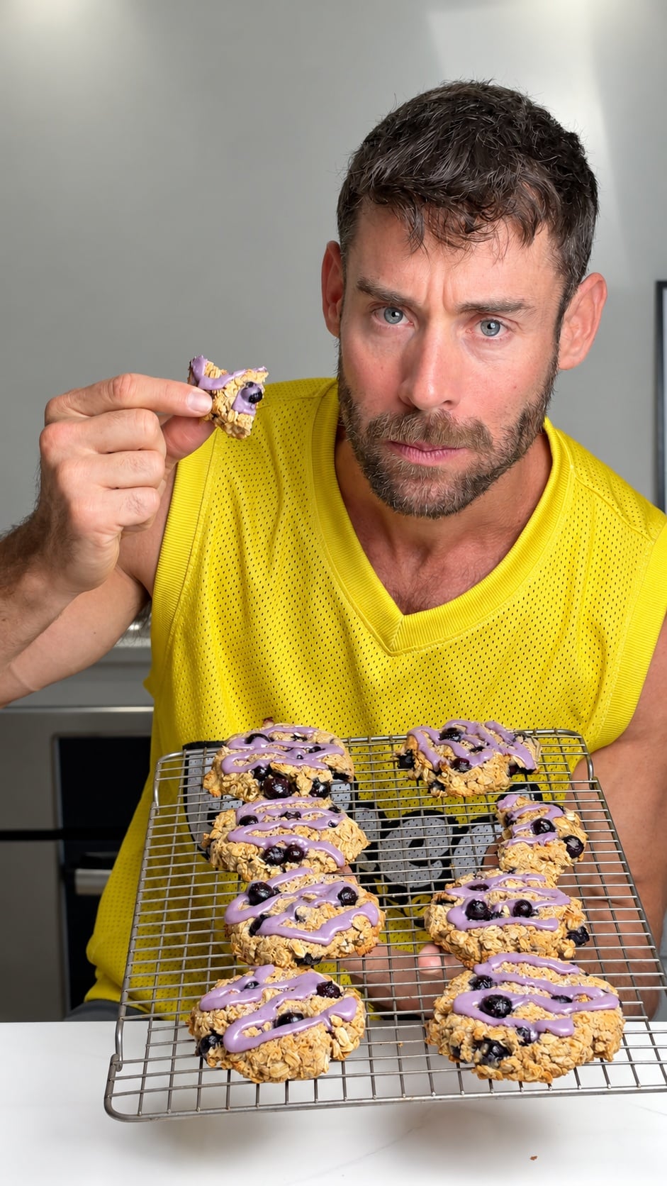 Jacob holding a broken glazed blueberry breakfast cookie over a tray of cookies