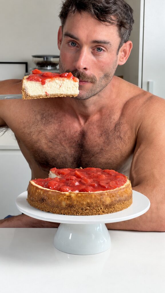 Jacob holding a slice of strawberry citrus cheesecake above the remaining cheesecake.