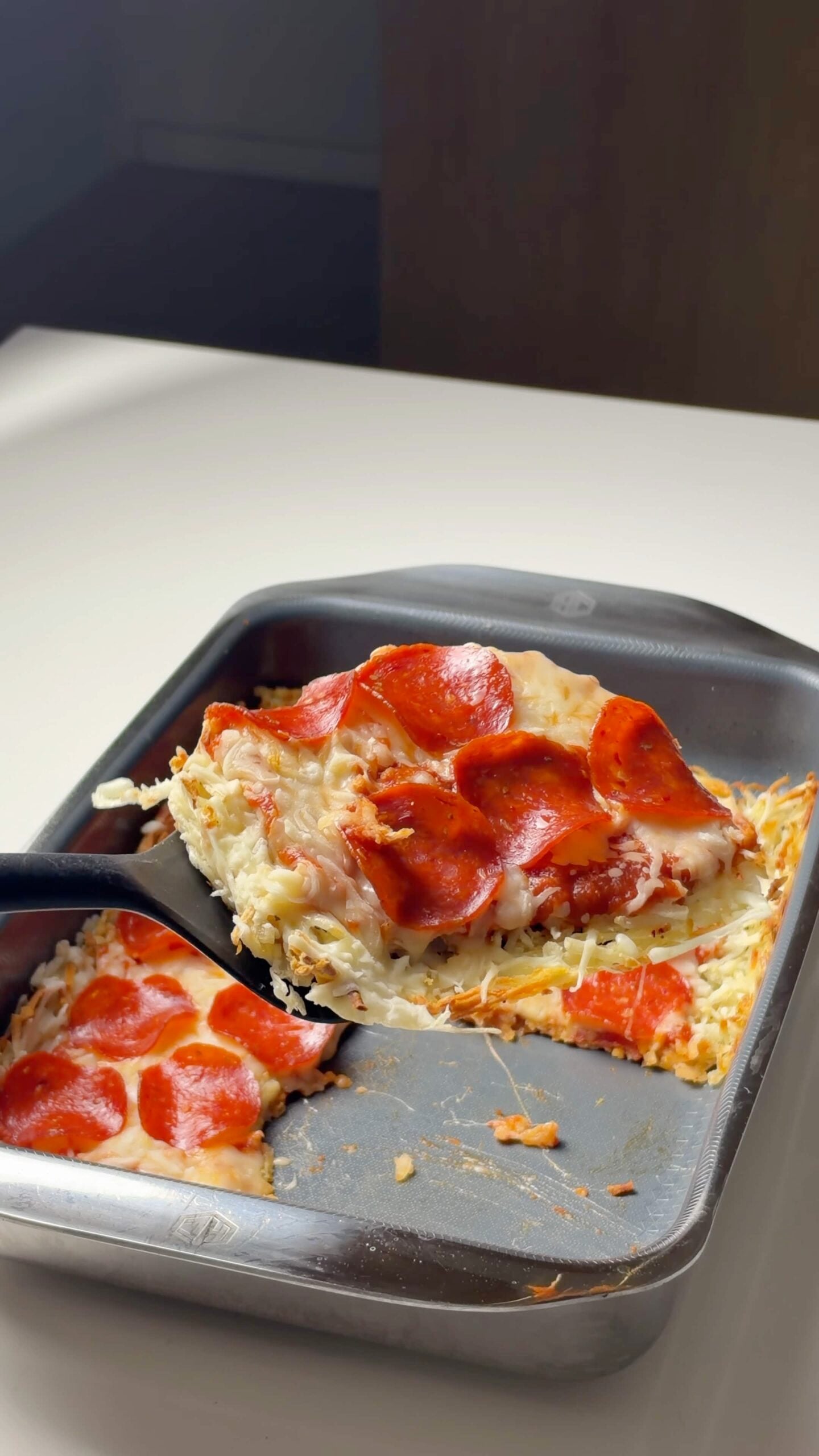 Hash brown pizza slice lifted from the pan to show the potato crust and melted cheese