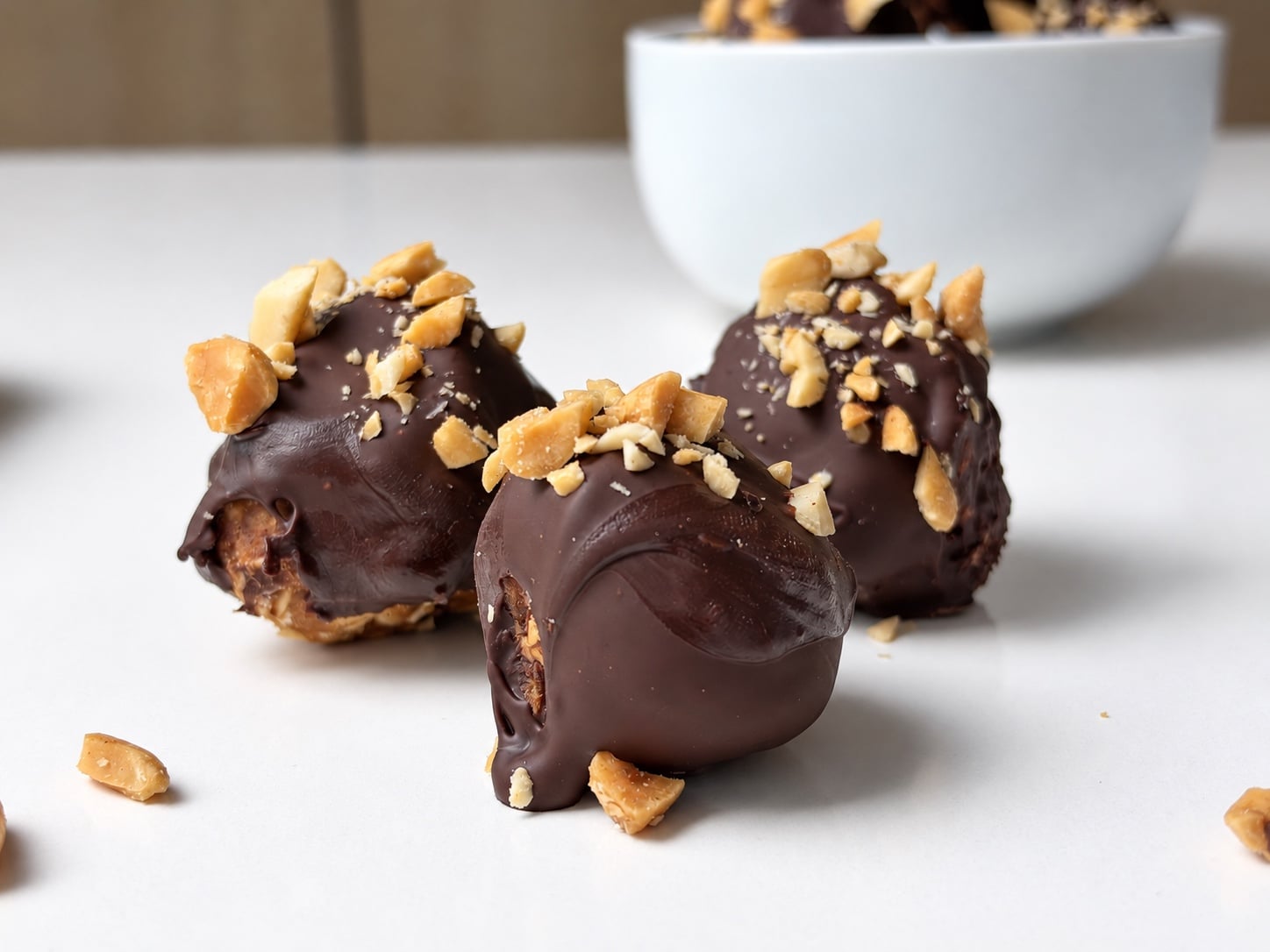Three chocolate-dipped peanut butter protein truffles topped with chopped peanuts