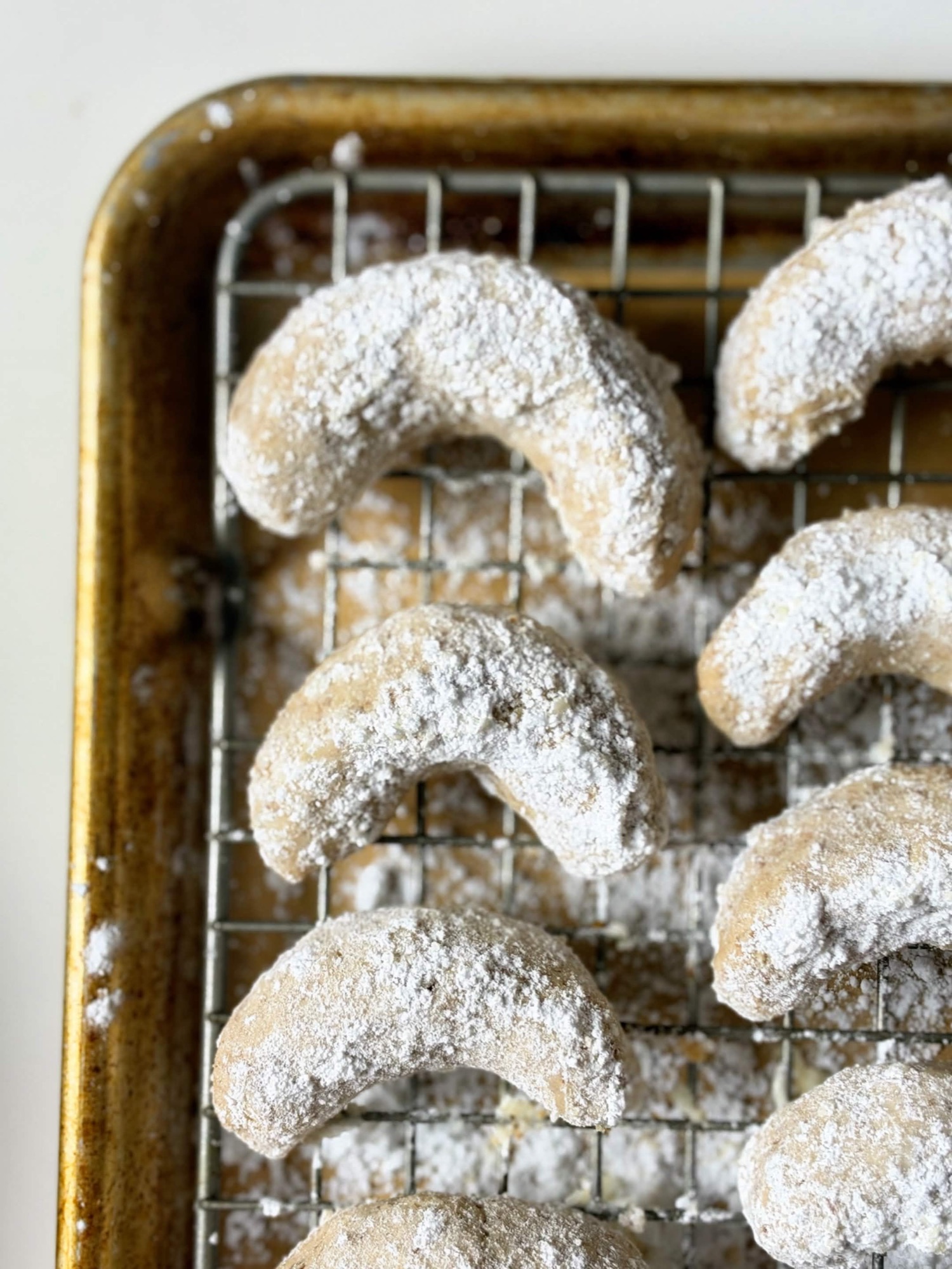 Powdered sugar-coated pecan crescent cookies cooling on a wire rack