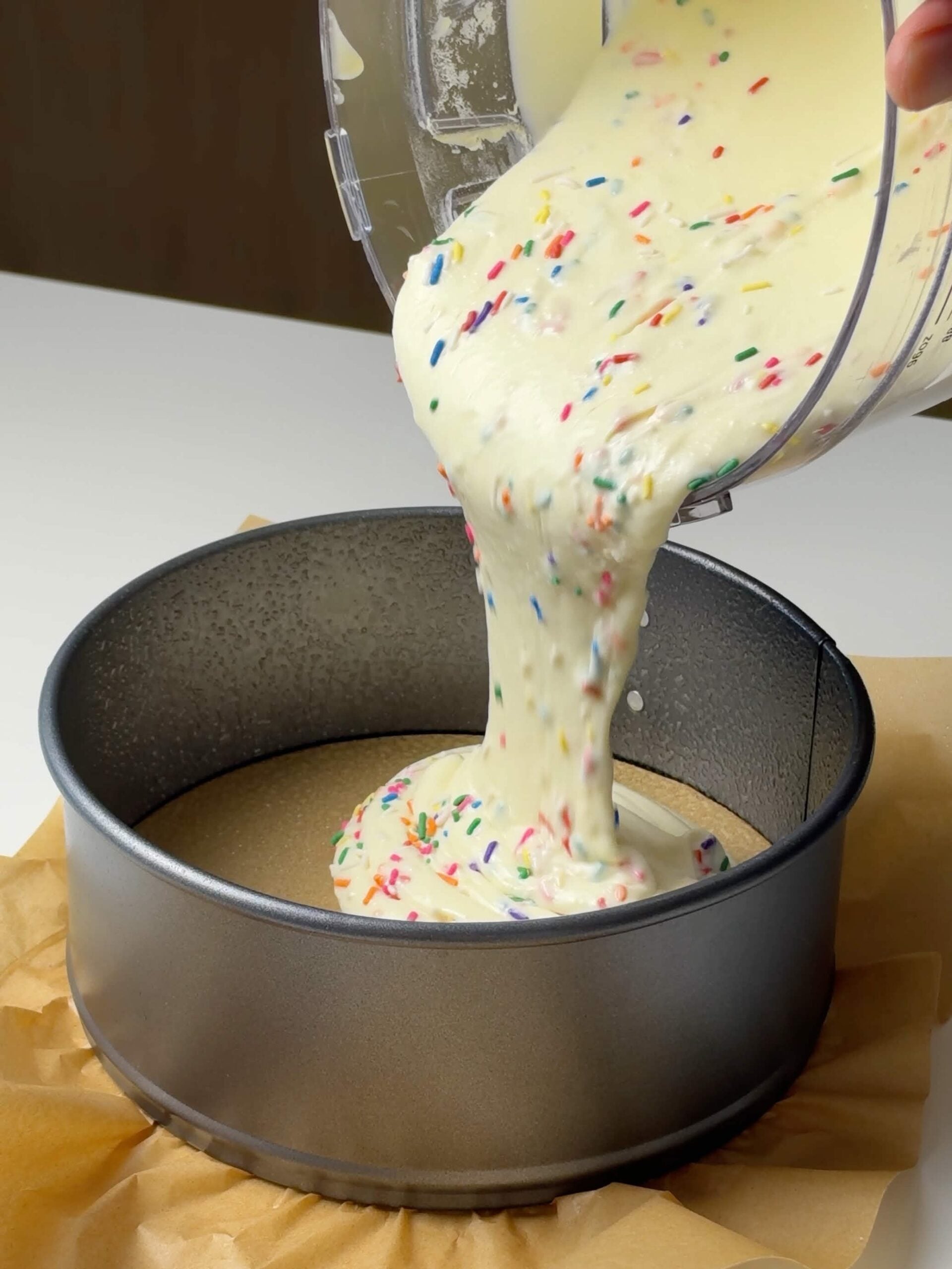 Sprinkle-filled birthday cake protein cheesecake batter being poured into a springform pan