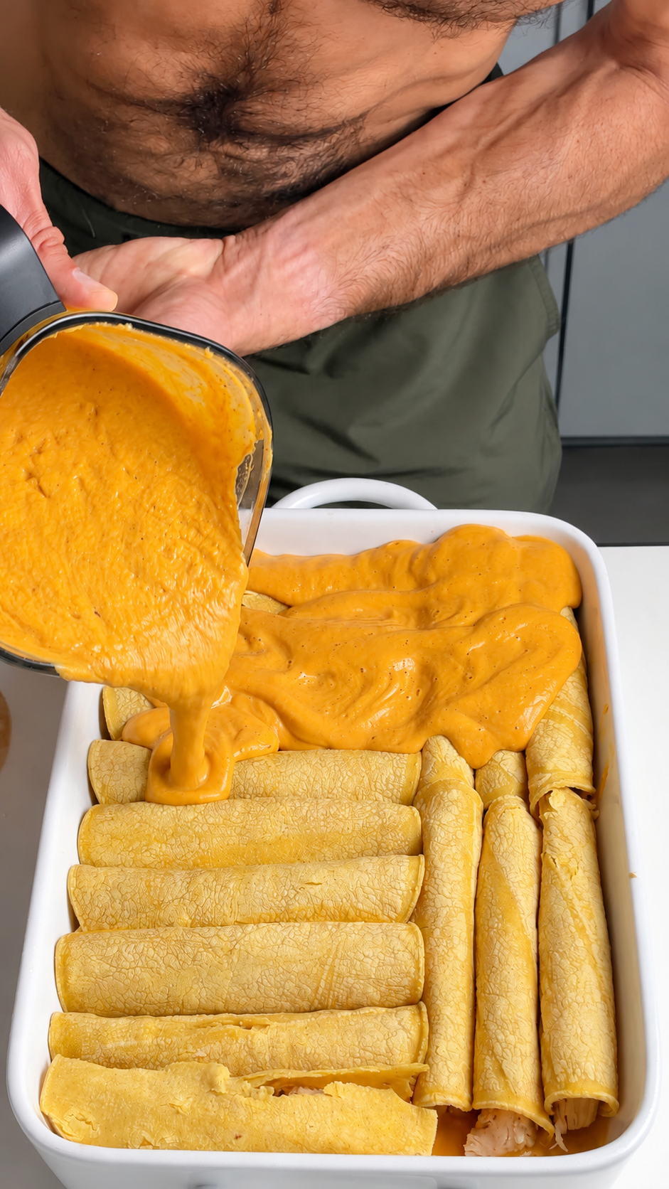Pumpkin cottage cheese sauce poured from a blender over rolled chicken enchiladas