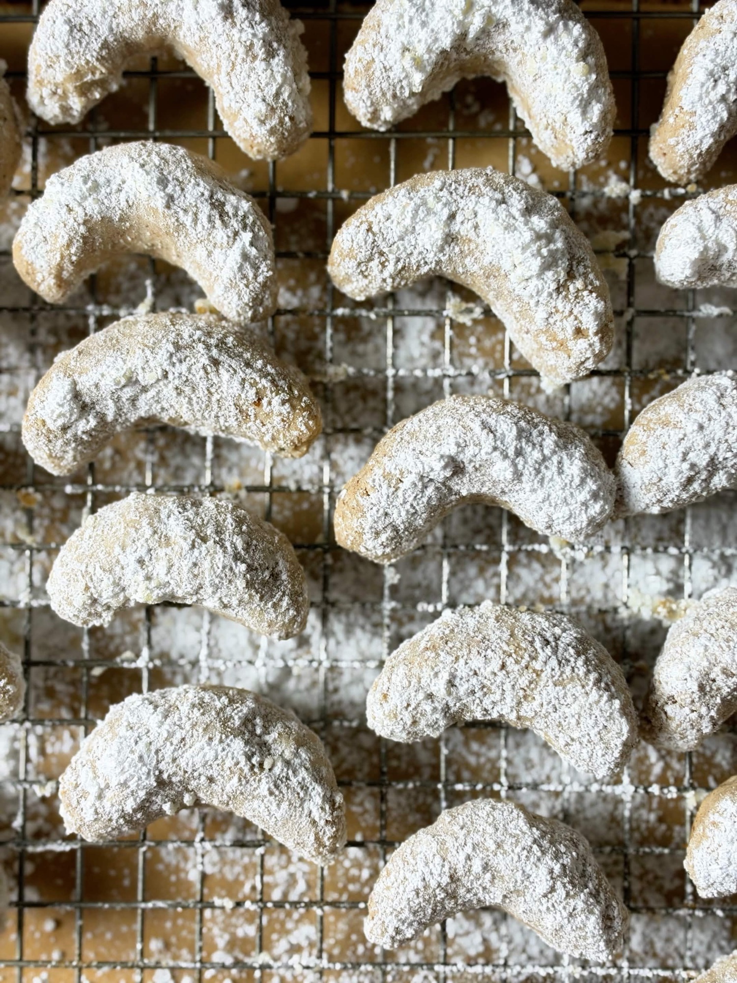 Close-up of powdered sugar-coated pecan crescent cookies on a wire rack
