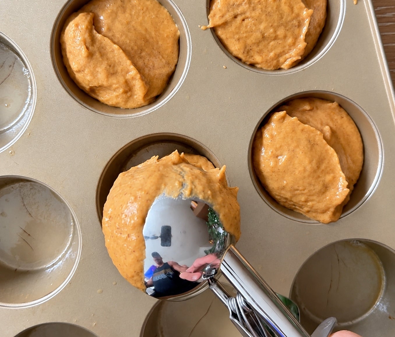 Portioning pumpkin protein muffin batter into a metal muffin tin with a scoop