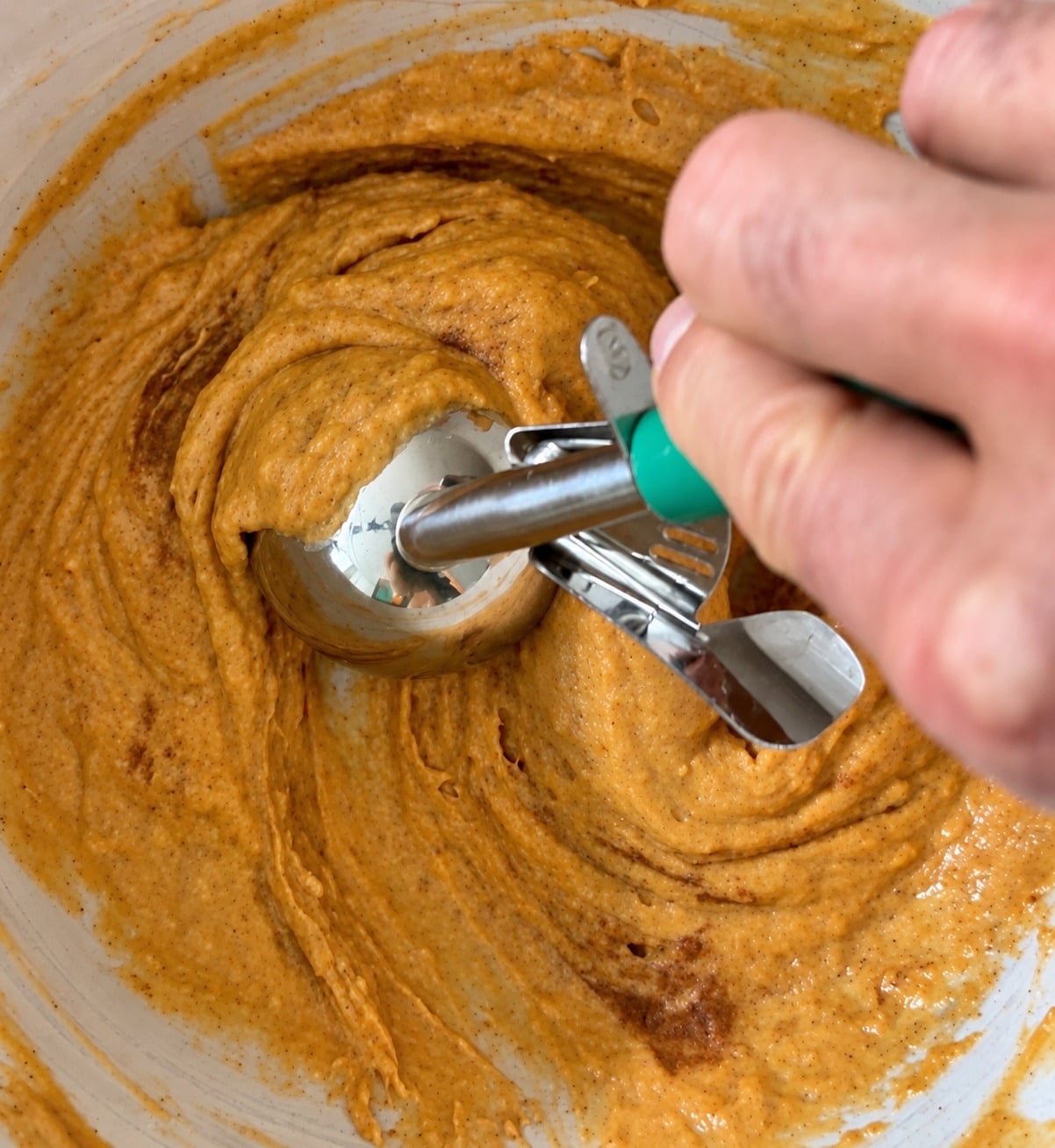Mixing thick pumpkin protein muffin batter in a bowl with a metal scoop