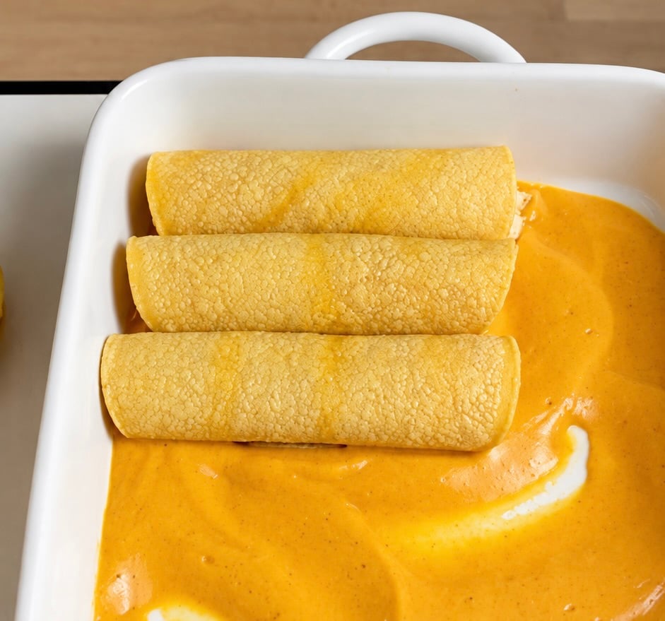 Three rolled corn tortilla enchiladas arranged over pumpkin sauce