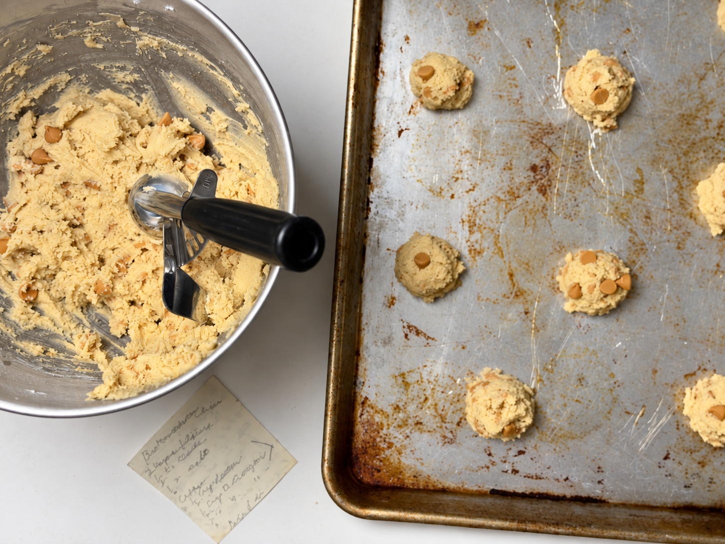 Overhead view of butterscotch cookie dough, a cookie scoop, and dough portions on a baking sheet