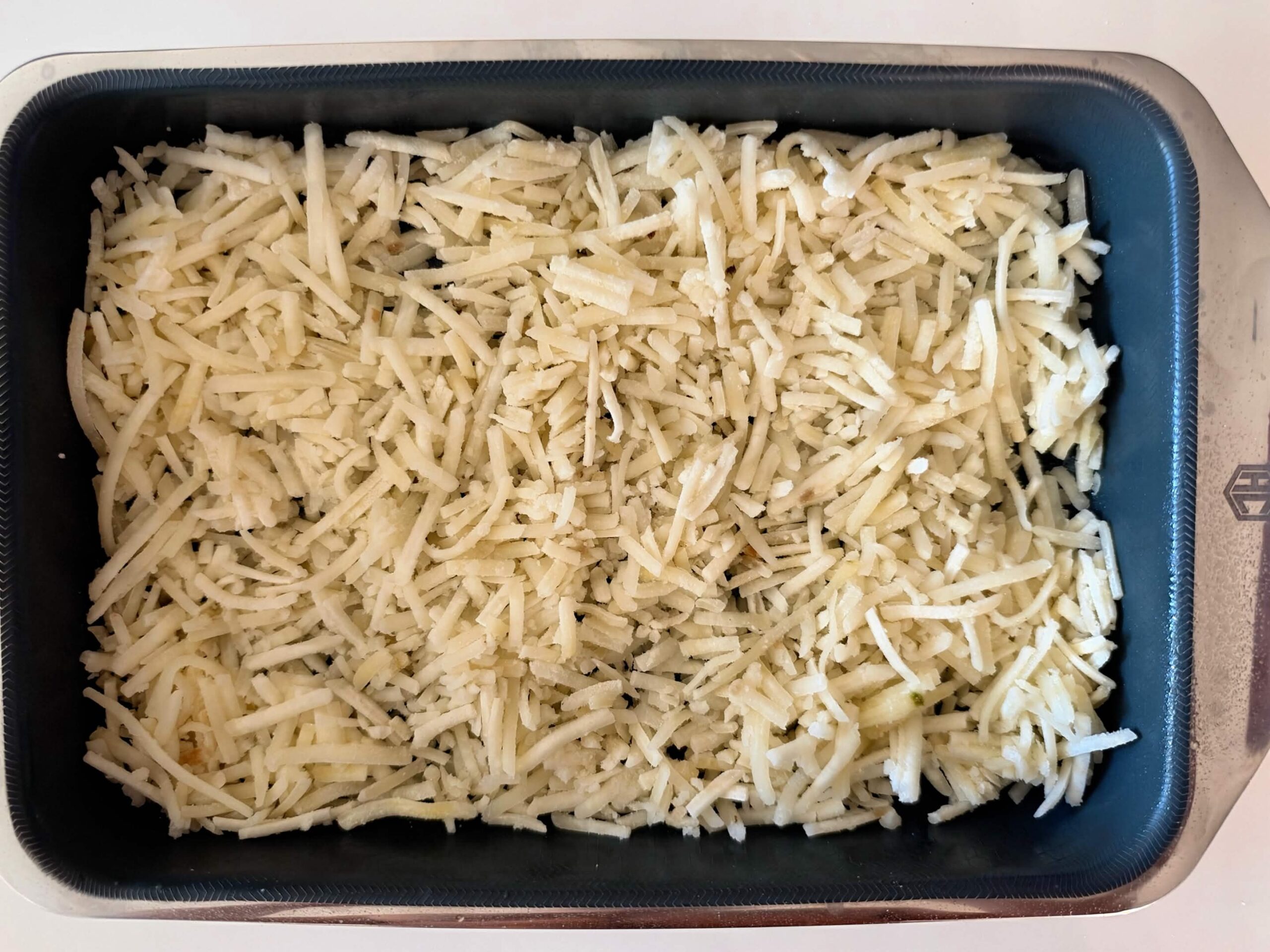 Frozen shredded hash browns pressed evenly into a metal baking pan
