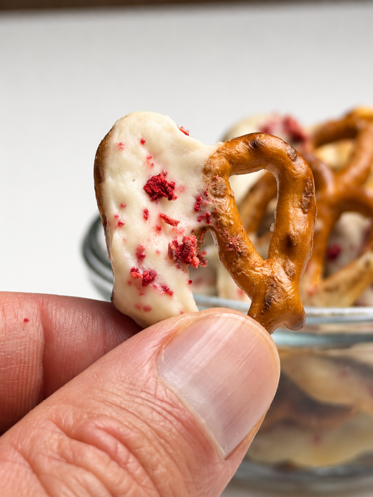 Close-up of a strawberry yogurt-covered pretzel held between two fingers