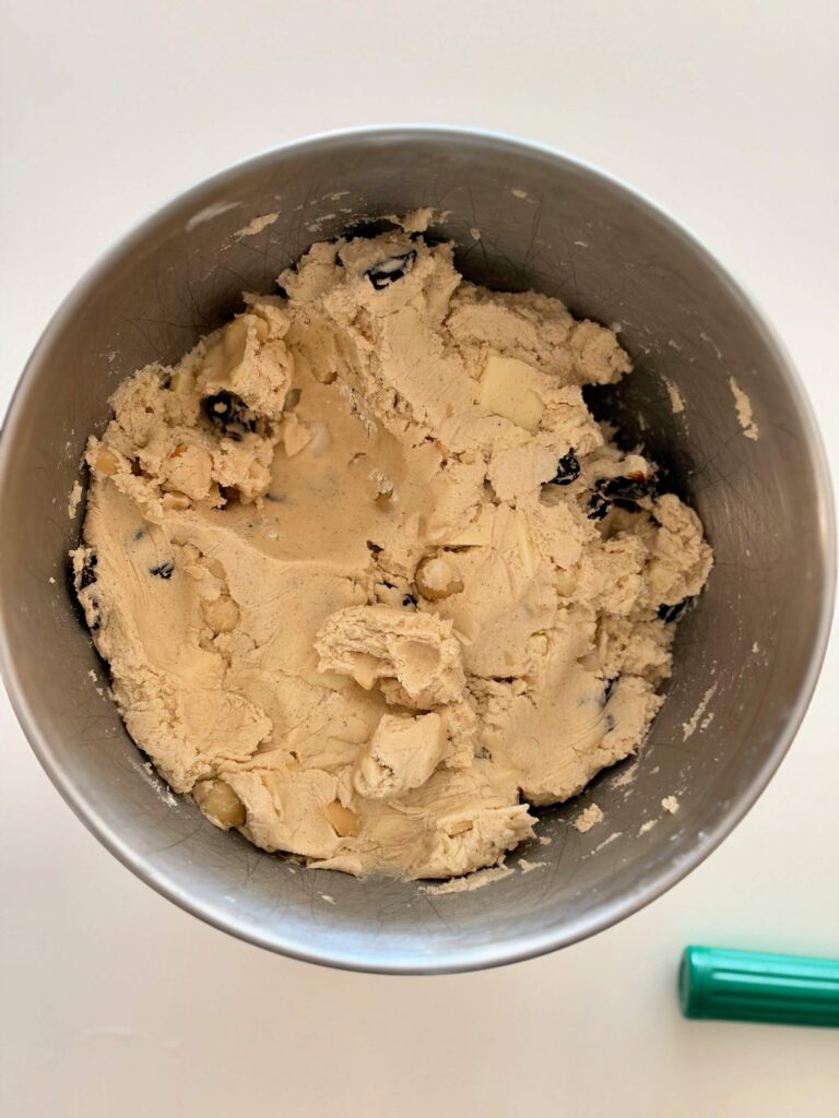 Gluten-free cookie dough mixed with white chocolate, dried tart cherries, and Marcona almonds in a metal mixing bowl.