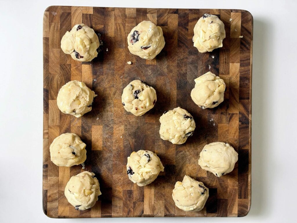 Large portions of white chocolate cherry almond cookie dough arranged on a wooden cutting board.