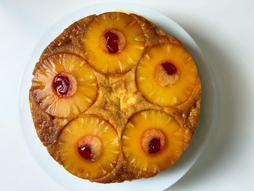 Overhead view of high-protein pineapple upside-down cake topped with five pineapple rings and maraschino cherries.