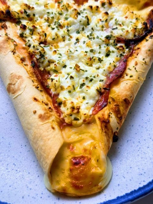 Close-up of a triangular personal pizza with cottage cheese, pepperoni, herbs, and melted mozzarella in the stuffed tortilla crust.