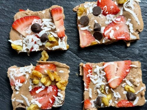 Four chocolate Greek yogurt bark squares topped with strawberries, walnuts, coconut, and chocolate chips