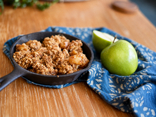 Gluten-free apple crisp baked in a cast iron skillet beside a whole and sliced green apple.