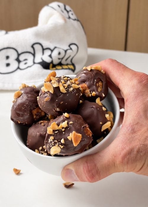 Hand holding a bowl filled with chocolate peanut butter protein truffles topped with chopped peanuts