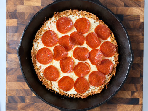 Overhead landscape view of high-protein hash brown pizza topped with melted mozzarella and turkey pepperoni in a cast-iron skillet.