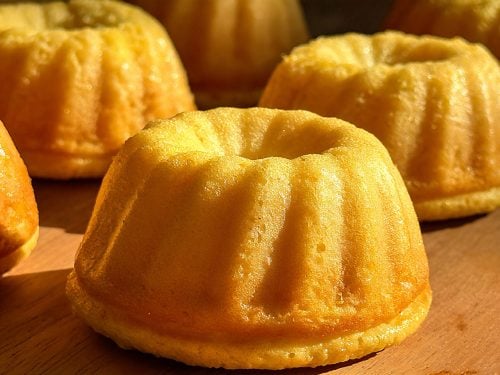Close-up of a golden, single high-protein whole orange mini Bundt cake on a wooden surface.