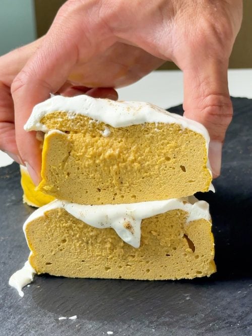 Hand holding two stacked slices of high protein pumpkin pie cheesecake