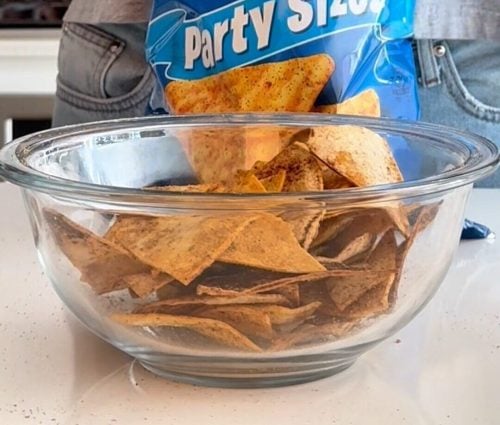 Glass bowl of homemade Cool Ranch Doritos in front of a blue Doritos bag for comparison.