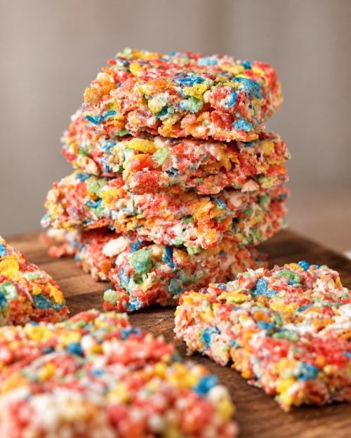 Tall stack of protein Fruity Pebbles rice crispy treats on a wooden board.