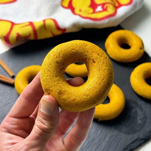 Hand holding a baked pumpkin spice donut with more donuts in the background