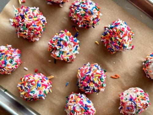 Several sprinkle-covered cake pops lined up on a baking tray
