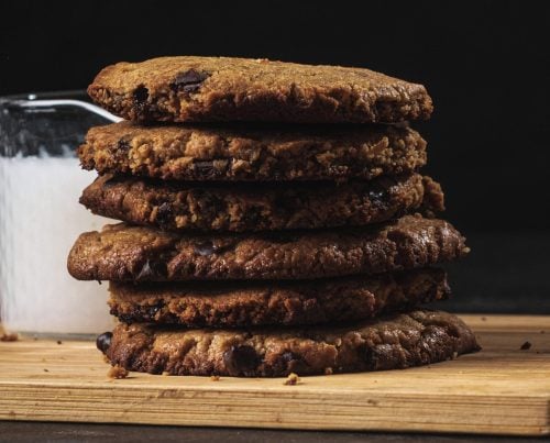 Vegan chocolate chip cookies stacked on a wooden board with a glass of milk
